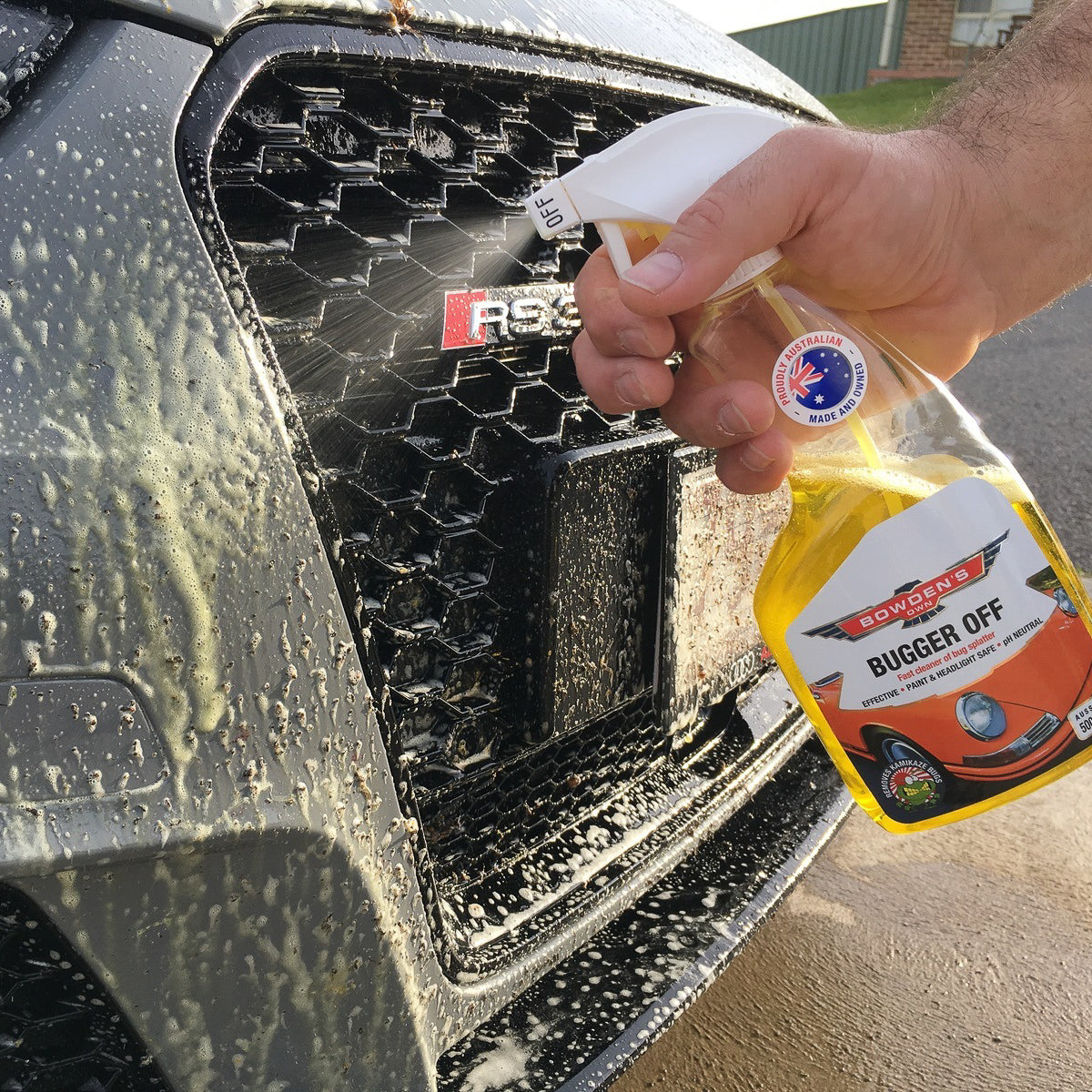 Person using a spray bottle labeled 'Bugger Off' on a car's grille.