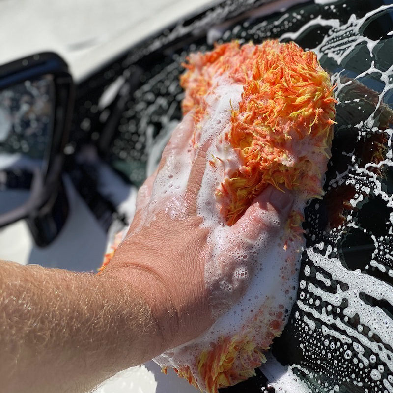 Hand holding a soapy orange sponge over a car being washed